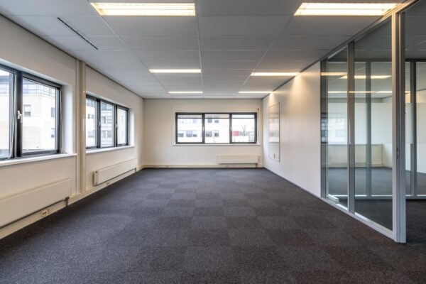 Lichte, lege kantoorruimte aan de Lage Biezenweg met grote ramen en glazen scheidingswand.